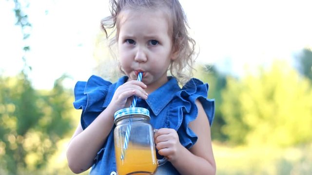 Child drinks orange fresh in the summer. Portrait of a little girl who enjoys smoothies through a tube