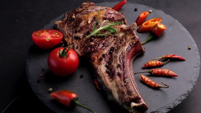 Grilled beef steak on bone with tomatoes rotating on the stone cutting board
