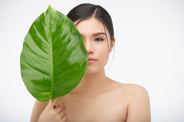 Young Asian woman with big green leaf closing face on white background