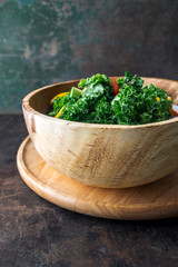 Kale salad in wooden bowl on rustic background