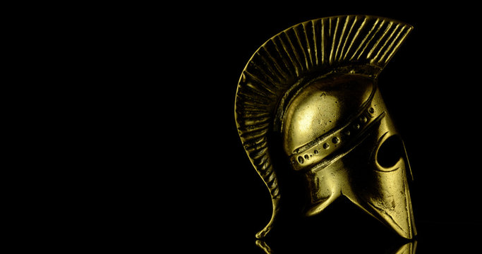 A wonderful golden Spartan helmet as part of the equipment of ancient greek soldiers. King Leonidas and his 300th The piece of metal stands against a black background