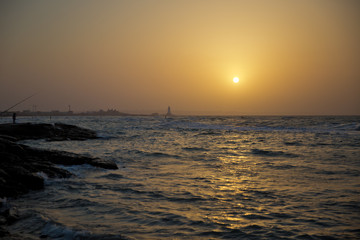 Obraz premium Beautiful sunset at the beach, amazing colors, light beam shining through the cloudscape. Azerbaijan sea and beach . The sound of the sea waves is coming . The fisherman fishes in the sea .