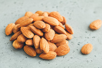 Heap of fresh almond nuts on a textured grey table.
