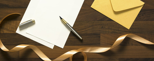 yellow envelope and blank white paper with pen on the wooden table with ribbon