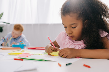 selective focus of multicultural preschoolers drawing pictures with pencils in classroom