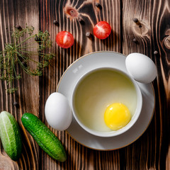 Separation the yolk of egg in little bowl, eggs, cherry tomatoes and fresh cucumbers on a wooden background with dill branche and allspice