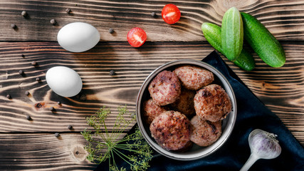 Fried meat patties in a bowl, two eggs, cherry tomatoes, garlic and fresh cucumbers on a wooden background with dill branche and allspice. Food concept