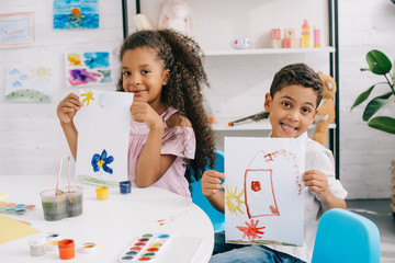 portrait of happy african american kids showing pictures at table in classroom