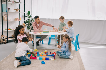 teacher and multicultural preschoolers on floor with colorful bricks in classroom