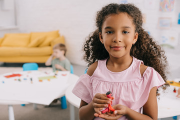 selective focus of african american kid with plasticine in hands and caucasian classmate behind in classroom