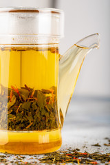 Green tea with strawberry flowers in teapot on gray table on light background