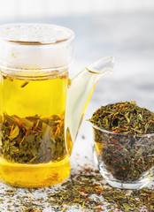 Green tea with strawberry flowers in teapot on gray table on light background