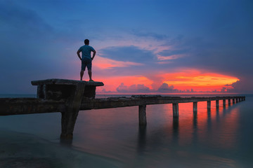 Man on bridge with sunrise over the beach