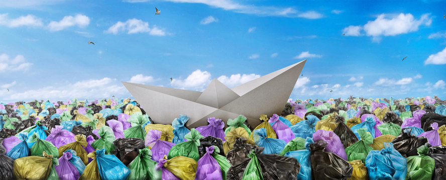 Concept of global pollution. A paper boat is floating on the sea of garbage on a sky background. Save the planet.