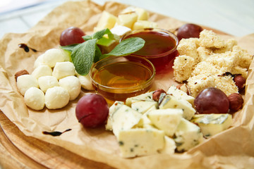 Maasdam, brie, camembert, roquefort cheeses on cheese board served with grapes, honey and sauce. Collection of  French and Italian cheeses on wooden board served with fruits. Isolated