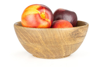 Lot of whole ripe deep red nectarine in a wooden bowl isolated on white