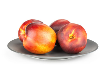 Lot of whole ripe deep red nectarine on a grey ceramic plate isolated on white