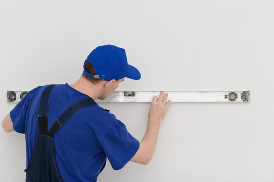 Worker in overalls measures the wall with a level