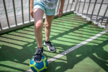 Knie eines Kindes mit Schürfwunde. der Fuß liegt auf einem Fußball