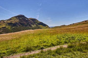 Fototapeta premium Summer view of Arthur's Seat in Holyrood Park with beautiful green grass and blue sky in Edinburgh, Scotland, United Kingdom.