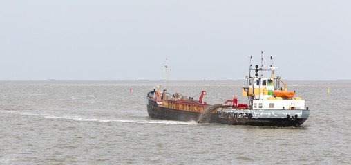 Naklejka premium Sand dredging boat drawing away from coast shoreline to pump sand