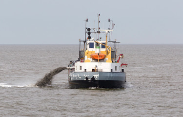 Sand dredging boat drawing away from coast shoreline to pump sand