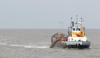 Sand dredging boat drawing away from coast shoreline to pump sand