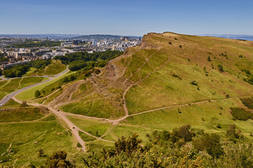 Summer view of Salisbury Crags from Arthur's Seat in Holyrood Park with beautiful green grass and blue sky in Edinburgh, Scotland, United Kingdom.