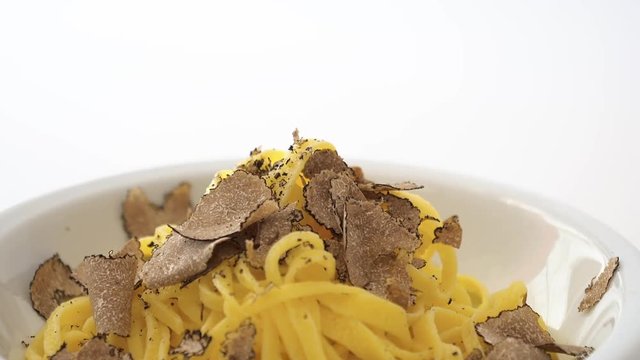 Fine grated black truffle falling on a plate of Italian fettuccine. Slow motion