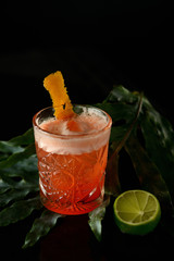 red cocktail with orange peel on a dark background