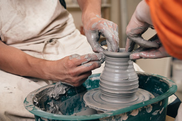 Man and woman hands pottery studying in studio. Creating vase. Hands in the clay and the potter's wheel with the product. Pottery class close up.