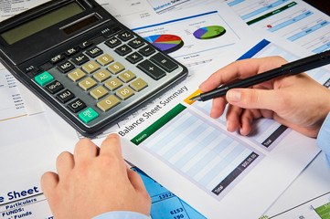 human hands write balance sheet summary on a background balances sheets with calculator