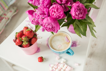 Gentle flowers are pink peonies, coffee with fluffy white milk foam and strawberries. The atmosphere of romance and pleasure.
