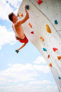 Photo of sportive man exercising on wall for climbing against cloudy sky
