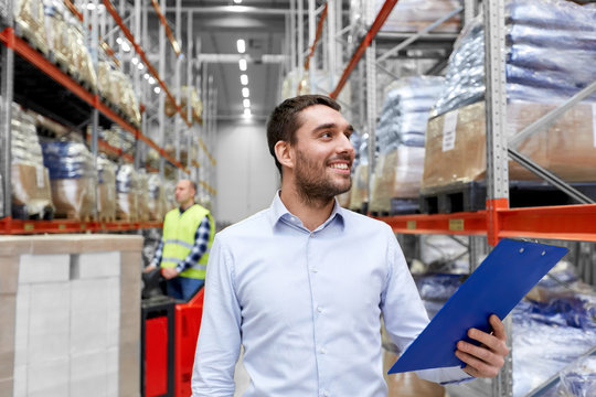 logistic business, shipment and people concept - happy businessman with clipboard and worker loading goods by forklift at warehouse