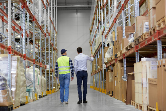logistic business, shipment and people concept - rear view of businessman and worker walking along warehouse