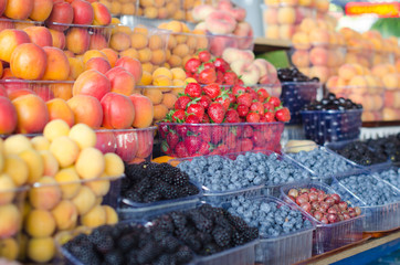 Containers with different ripe berries and fruit at market