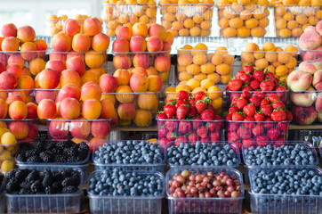 Containers with different ripe berries and fruit at market