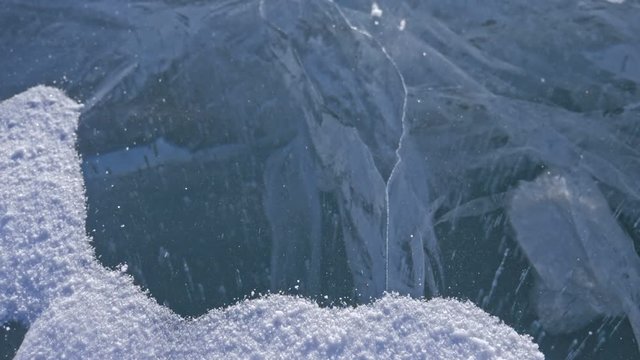 Snow is flying over surface of ice. Snowflakes fly on ice of Lake Baikal. Ice is very beautiful with unusual unique cracks. Snow sparkles and glows in red. Shooting slow motion 180fps. Picture at