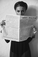 Black and white portrait of beautiful woman in newsboy cap with vintage newspaper in hands. Retro...