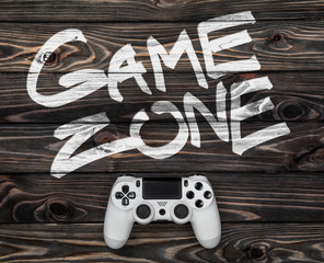 white gamepad on a dark wooden background. phrase game zone written in white