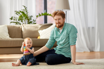 family, fatherhood and people concept - happy red haired father with ball playing with little baby daughter at home