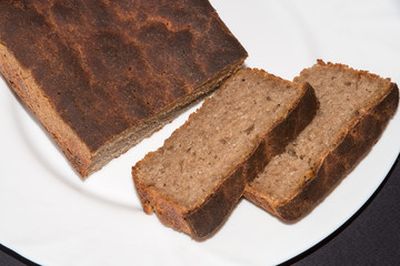 Black rye bread sliced in plate on dark table. Freshly baked homemade rye and white flour bread. Close up. Copy space.