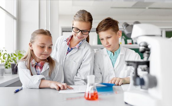 education, science and children concept - happy kids with workbooks studying chemistry at school laboratory