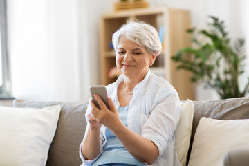 technology, communication and people concept - happy senior woman with smartphone at home