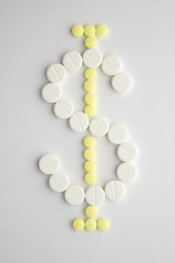 the high cost of medicines: Tablets of different colors are laid out on white in the form of a dollar symbol