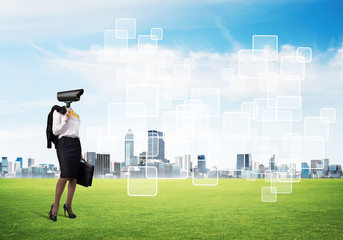 Camera headed woman standing on green grass against modern cityscape