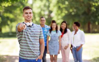 people, friendship and international concept - happy smiling man with headphones pointing at you and group of happy friends outdoors