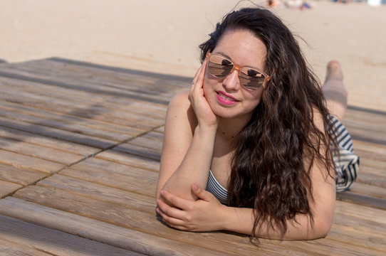 Woman with sunglasses lying on the wooden boardwalk on the beach