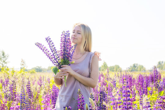Beautiful woman with bouquet of lupines on the field